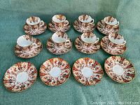 Full view of 8 tea cups and 12 saucers showing ornate floral and gold pattern with all items laid out carefully