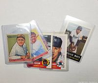 Front view of four vintage baseball cards in protective sleeves featuring George Herman Ruth, Hank Aaron, New York Yankees player, and Willie Mays.