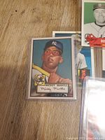 Close-up photo of Mickey Mantle baseball card in protective sleeve on wooden surface.