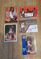 Five Michael Jordan basketball cards arranged on wooden surface, two with visible autographs, colorful backgrounds and player images.