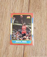 Front of the Michael Jordan 1986 Fleer basketball rookie reprint card showing Jordan in red Chicago Bulls uniform mid-air for a dunk with vibrant red border and Fleer logo in top right.