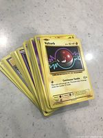 Stack of assorted Pokemon trading cards with Voltorb on top showing 60 HP and Continuous Tumble attack.