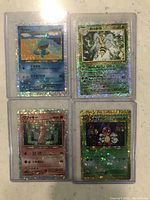 Photo of four Japanese holographic Pokémon cards in protective sleeves showing Wooper, Beedrill, Clefairy, and Wurmple.
