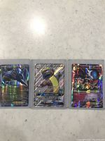 Top-down image showing three holographic Pokémon cards in protective sleeves (Marshadow GX, Dusknoir GX, Mega Gardevoir EX).