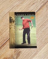 Front view of the 1997 Tiger Woods rookie card showing Tiger wearing a red sweater with putter, gold foil text on side.