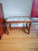 Front angled view of vintage wooden side table with lace top under glass, showing turned legs and floor.