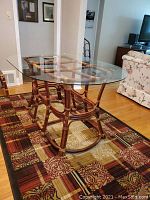 Oval glass top table with bamboo pedestal base on a patterned rug, in a living room area.
