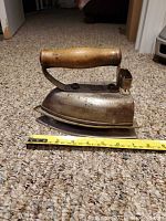 Side view of the vintage iron showing wooden handle and metal body with tape measure indicating length of about 7 inches.