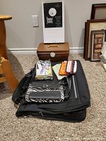 View of assorted ladies items including garment bag, purses, knitting and sewing notions, and toiletries shown on carpeted floor.