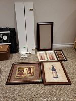 Photo showing two white 36 inch shelves standing against wall with mounting hardware wrapped in plastic, several framed pictures laid on carpet including wine bottle art, bicycle scene, and floral prints.