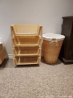Photo of 4 beige plastic stacking baskets beside tall wicker hamper with liner on carpeted floor