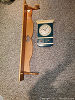 Wood shelf/quilt rack with decorative cutout on the back panel and dowel holders, shown next to the wall clock on carpeted floor.