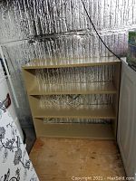 Front view of beige painted metal shelving unit with 4 shelves, showing some wear and open back panel.