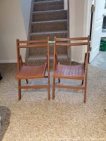 Front view of two wooden folding chairs side by side on carpeted floor in basement.