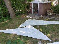 Two white jib sails laid flat on grass in front of a shed shown from a distance to demonstrate size and shape.