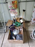 View of box containing assorted garden and entertaining items including tools, watering cans, flags, and cast iron accessories.