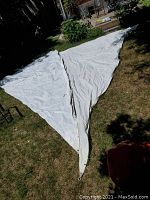 Two white sailcloth sails laid out on grass, triangular shape, visible grommets