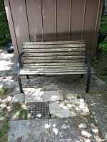 Photo of full garden bench showing weathered wooden slats and metal frame on stone pavement.