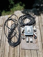 Photo of electrical panel mounted on plywood with 12 outlets attached around it plus two heavy-duty cords coiled next to it.