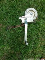 Full view of manual winch showing crank handle, gear, chain, and hook lying on grass.