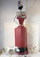 Full view of large paper-mache Calaca figure with red dress and skeletal arms, two skeletal pets at base.