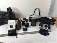 Overview of the lot showing cameras, lenses, lens caps, and camera bags laid out on a surface.