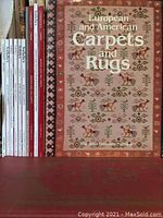 Books and auction catalogues about carpets and rugs, including a book titled "European and American Carpets and Rugs" with a reddish cover and intricate carpet pattern.