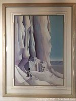 Framed print showing stylized landscape with large rock formations and Pueblo-style structure.