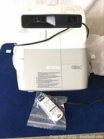 Front view of projector with remote control in plastic bag and power cable visible