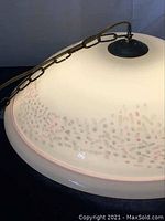 Close-up side view of the translucent white Murano glass dome lamp with pink and beige speckled pattern and metal chain mounted on top.
