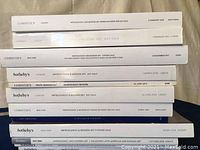 A stack of 9-10 auction sale catalogs with visible spines showing Sotheby's and Christie's branding and dates mostly from 2005 to 2019.