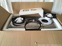 Two burner stainless steel hot gas plates with black burner grates, accessories, and packaging inside a cardboard box