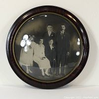 Front view of antique black and white family portrait in round wooden frame with reflective convex glass.