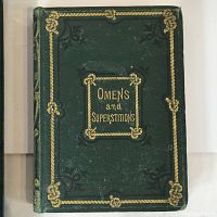 Front cover of 'Omens and Superstitions' book, showing green embossed hardcover with gold detailing.