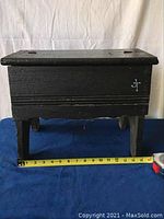 Closed vintage black wooden shoe polishing box on four legs, showing dimensions with measuring tape