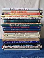 Books stacked vertically showing titles related to watercolor painting techniques and artists.