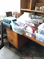 Photo showing the area with several plastic containers and cases on a wooden desk, containing various tools and accessories, including battery bins and smoke alarms
