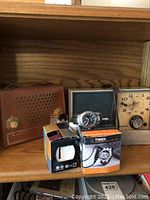 Group photo showing all items on shelf, including a vintage Heathkit transistor radio in brown leather case, Westinghouse desk clock, Timex Ironman watch in box, Caprice wrist watch in white box, and Timex men's leather band watch.