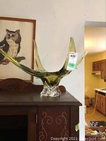 Full view of the retro green four-point glass vase with clear base, positioned on a table with background featuring framed artwork.