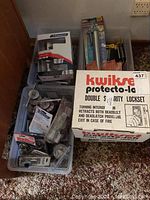 Plastic bin with various lock hardware and locked packaging with Kwikset Protecto-lok box.