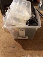 Photo showing transparent plastic bin containing two clear lure holders, camouflage lunch bag, and fishing gear inside.