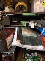 Photo showing the 14x14 dome screen house in red and black Outbound carry bag, three rolls of fiberglass screening, and green packaging for a DIY outdoor antenna on a metal shelf.