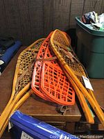 Full view of three pairs of snowshoes; two wooden ones and one orange plastic pair