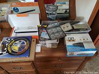 Various items on a wooden dresser including the Goodyear 100th anniversary book, white boxes, remotes, and other accessories.