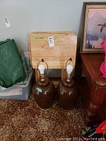 Photo showing four light-colored wooden tray tables in various conditions including one shrink wrapped and one with damage, along with two brown ceramic lamps with bulbs but no shades.