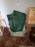 Green tarp folded inside clear plastic storage bin, tarp appears large with grommets visible
