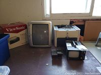 View of entire lot with boxed projector, printer, two flip phones, and two CRT TVs on floor