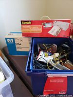 Photo showing HP LaserJet 96A printer cartridge box, Scotch thermal laminator in original packaging, and blue tote filled with assorted cables and accessories