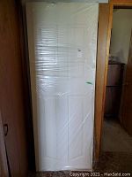 Off-white solid door wrapped in plastic with four recessed rectangular panels