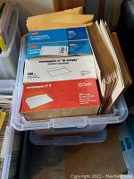 Two plastic bins filled with various envelopes in boxes and loose, including manila, white, and larger sizes.